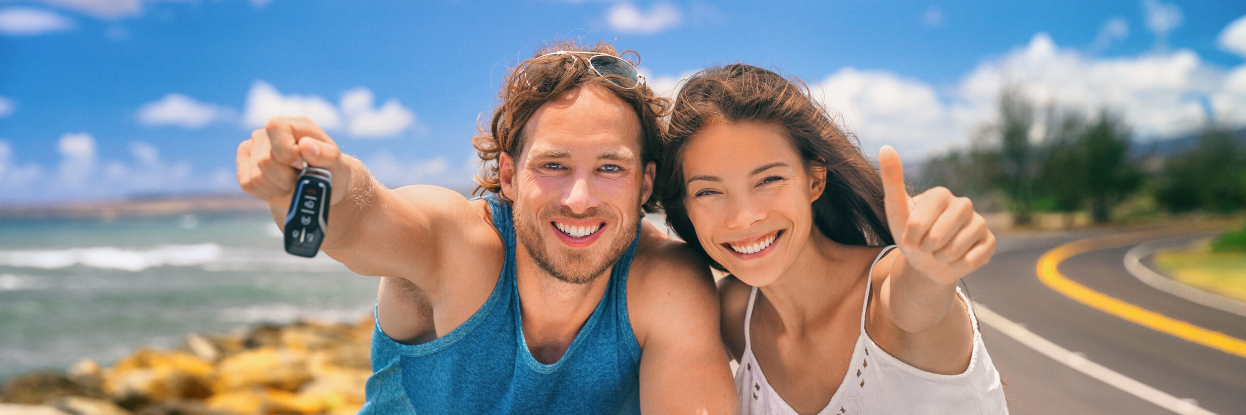 Ein man und eine Frau halten Daumen und Autoschlüssel hoch und lächeln.